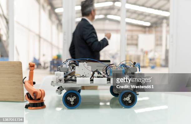 model of robotic arm and vehicle on desk with businessman standing in background at factory - smart car stockfoto's en -beelden