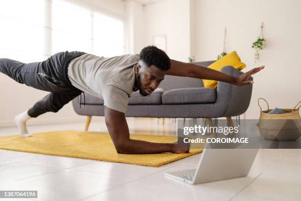 man watching online exercise video on laptop while working out in the living room at home. - man living room stockfoto's en -beelden