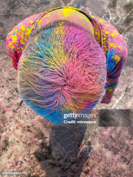 bild eines hinduistischen indischen mannes auf dem dach, der mit farbpulverfarbe bedeckt ist, sich bückt und haare zeigt, die mit buntem gulal bedeckt sind, beim holi-festival der farben und des liebesmalkampfes herumspielt, erhöhte aussicht - farbpulver stock-fotos und bilder