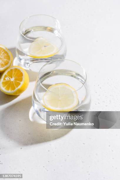 two glasses of water with lemon on wight table with hard light and shadow. - hard liquor stock pictures, royalty-free photos & images