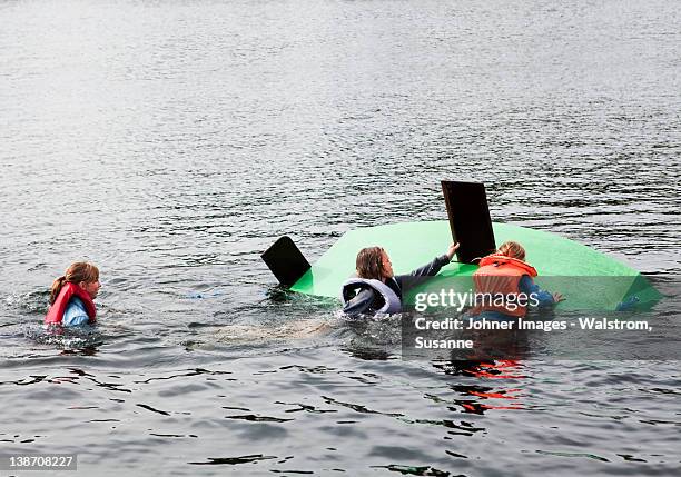 three children swimming around capsized sailing dinghy - capsizing photos et images de collection