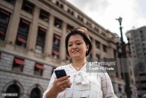 donna d'affari matura che utilizza il telefono cellulare in città - mature asian woman candid foto e immagini stock