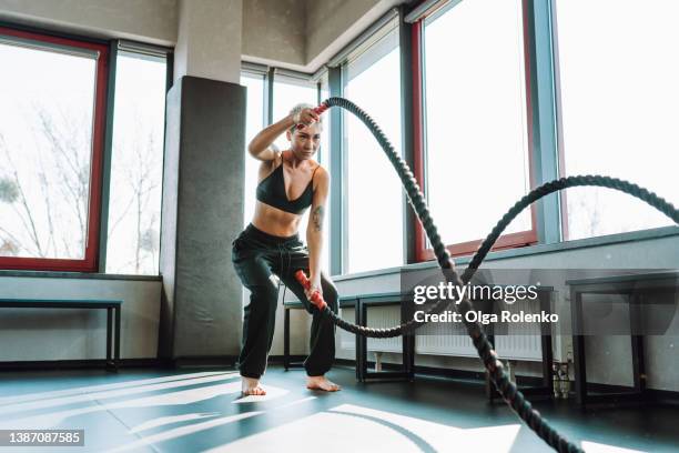 woman with short hair exercising with battle ropes. strong woman do workout at gym - crossfit stockfoto's en -beelden