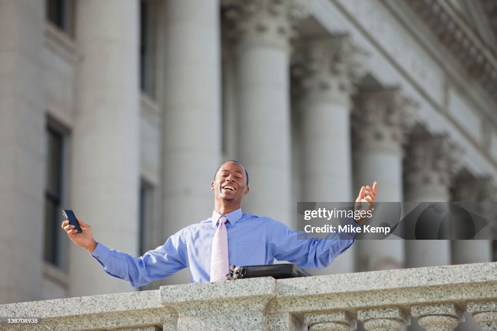 Black businessman holding cell phone with arms outstretched