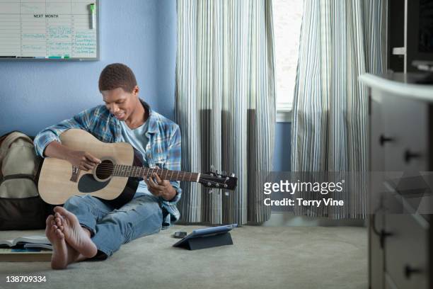 mixed race teenage boy strumming guitar - teen boy barefoot 個照片及圖片檔