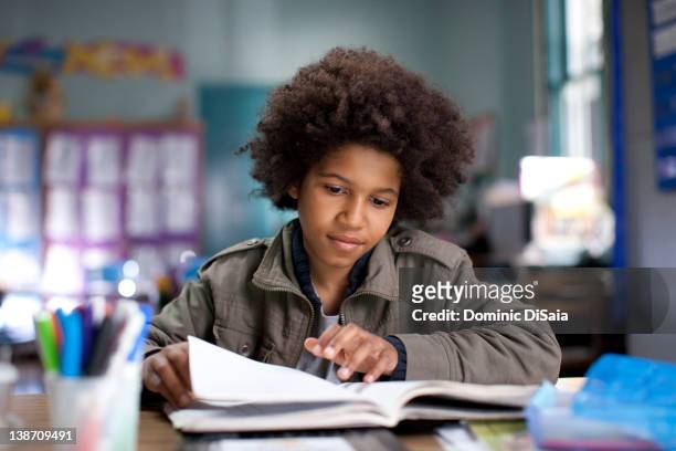 african american boy studying in classroom - boy reading a book stock-fotos und bilder