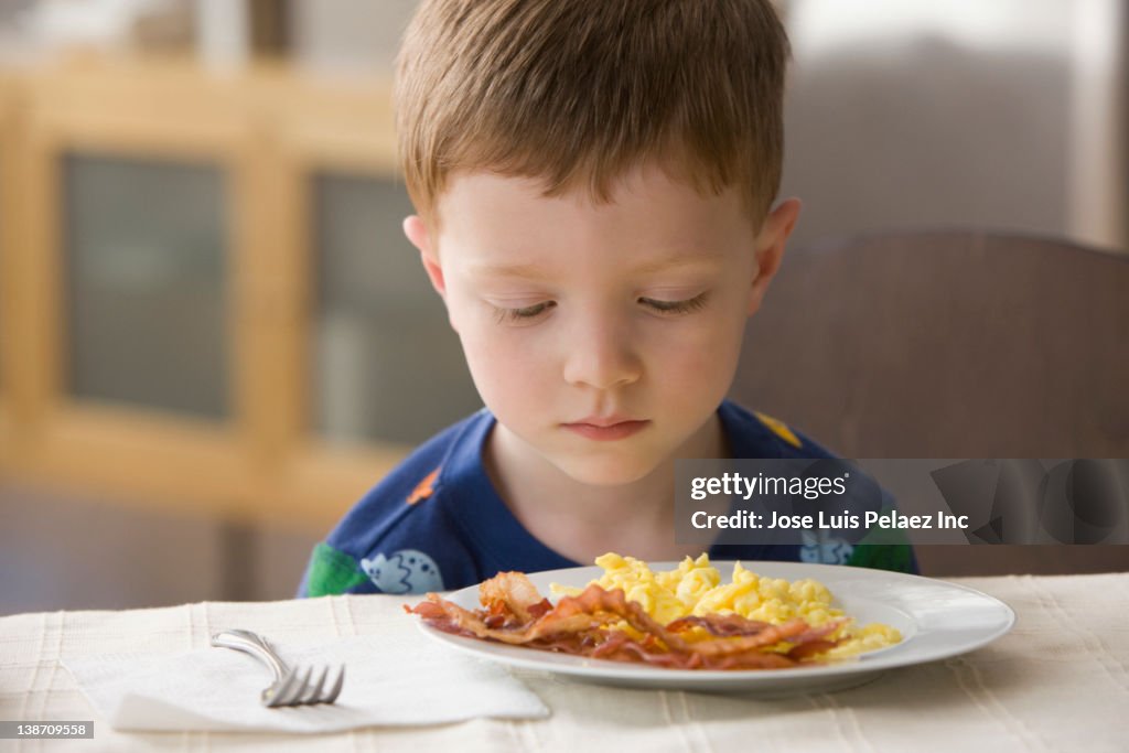 Caucasian boy looking at plate of eggs and bacon