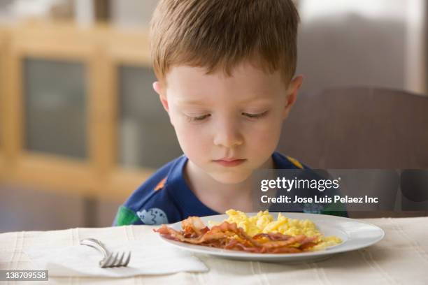 caucasian boy looking at plate of eggs and bacon - refusing stock pictures, royalty-free photos & images