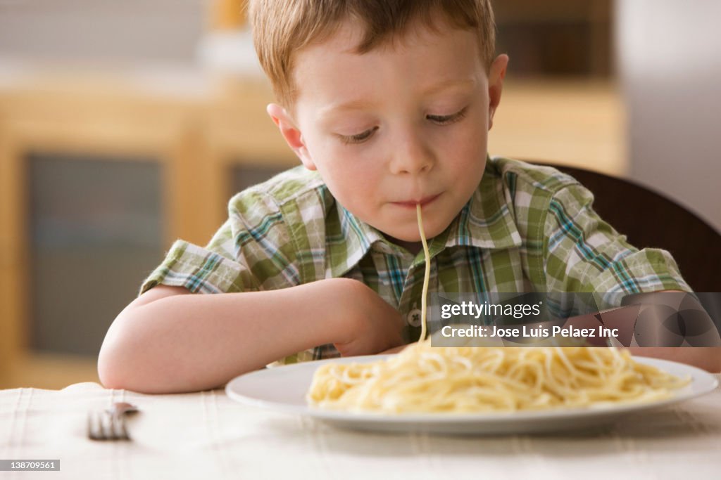 Caucasian boy eating pasta noodle