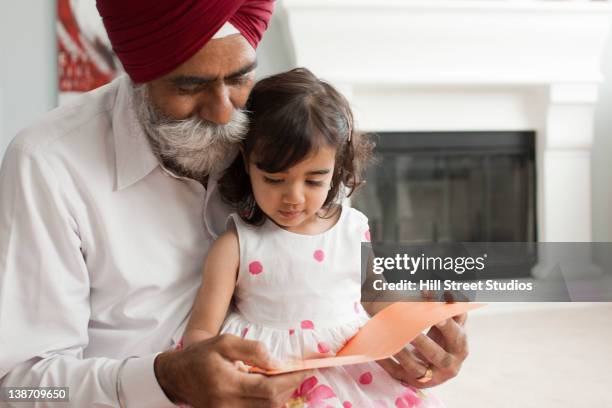 asian grandfather reading book to granddaughter - sikh fotografías e imágenes de stock