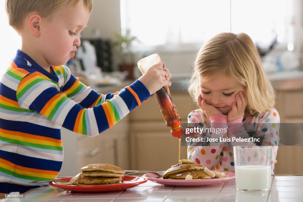 Caucasian boy pouring syrup on sister's pancakes