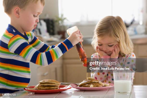 caucasian boy pouring syrup on sister's pancakes - pancake day foto e immagini stock