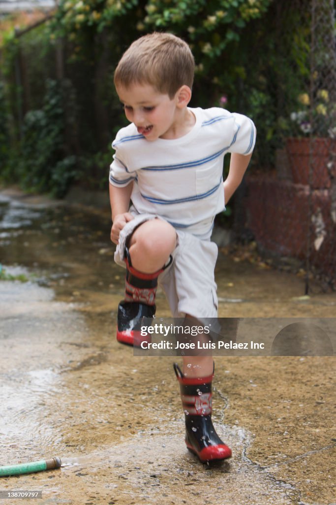 Caucasian boy stomping in water puddle