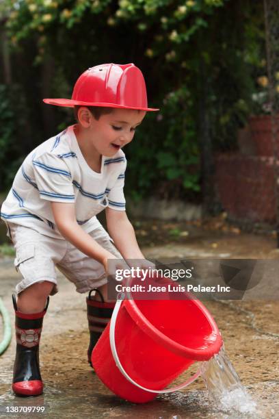 caucasian boy playing with bucket wearing fireman's hat - boy fireman costume stock pictures, royalty-free photos & images