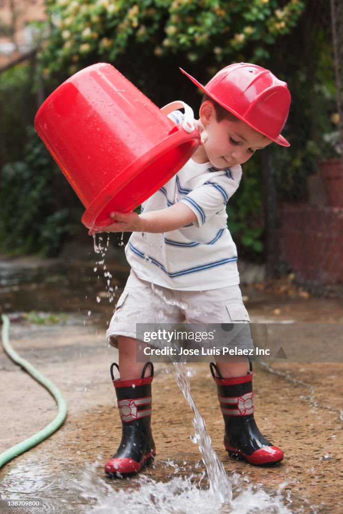 Caucasian boy playing with bucket wearing fireman's hat