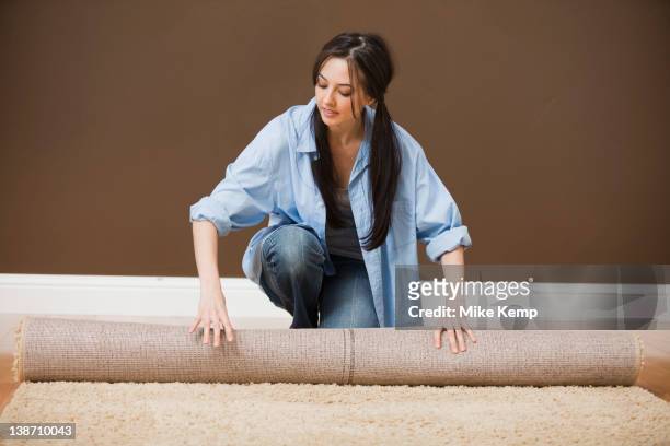 caucasian woman unrolling carpet - carpet roll stock-fotos und bilder