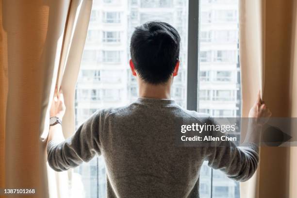 the asian man opened the curtains and looked out of the window - rear view hand window stock pictures, royalty-free photos & images