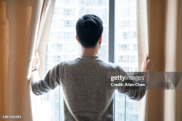 the asian man opened the curtains and looked out of the window - pulling stockfoto's en -beelden