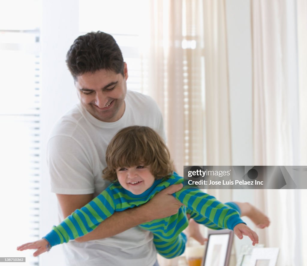 Mixed race father swinging son in bedroom