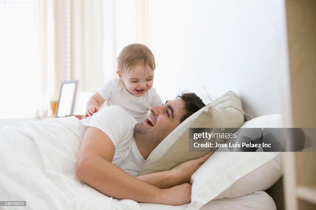 Mixed race father and baby boy playing in bed