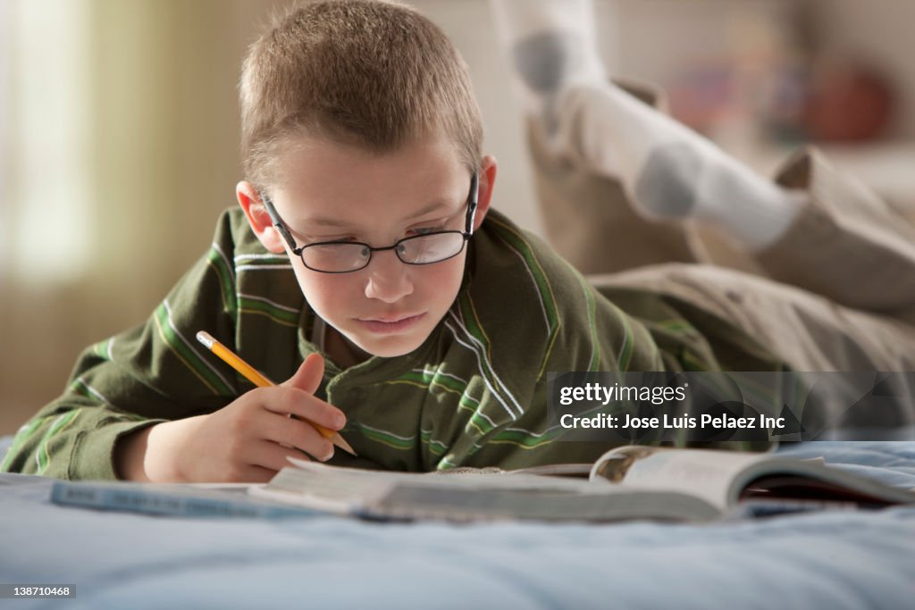 Caucasian boy laying on bed studying