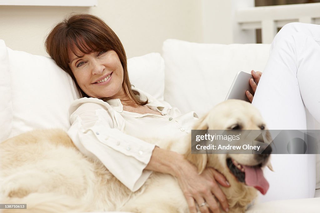 Woman sitting with dog on sofa using digital tablet