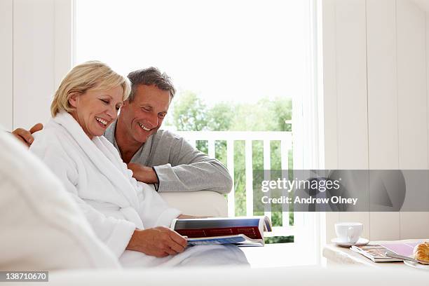 couple in bathrobes looking at magazine together - magazine retreat day 2 stock pictures, royalty-free photos & images