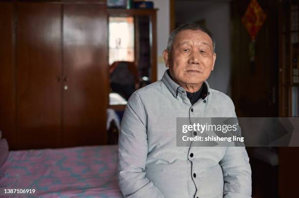 il vecchio solitario dell'asia orientale si sedette sul letto della sua camera da letto e guardò la macchina fotografica. - popolazione dellasia orientale foto e immagini stock
