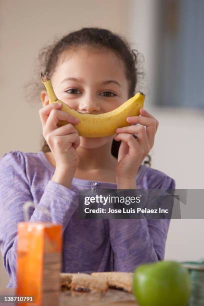 hispanic girl eating banana for lunch at school - banane essen stock-fotos und bilder