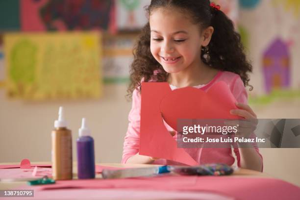 hispanic girl cutting out valentine's heart in classroom - kunst en nijverheid stockfoto's en -beelden