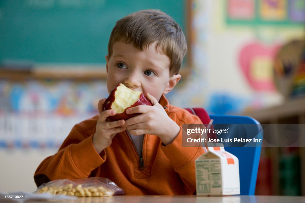 Caucasian boy eating lunch in classroom