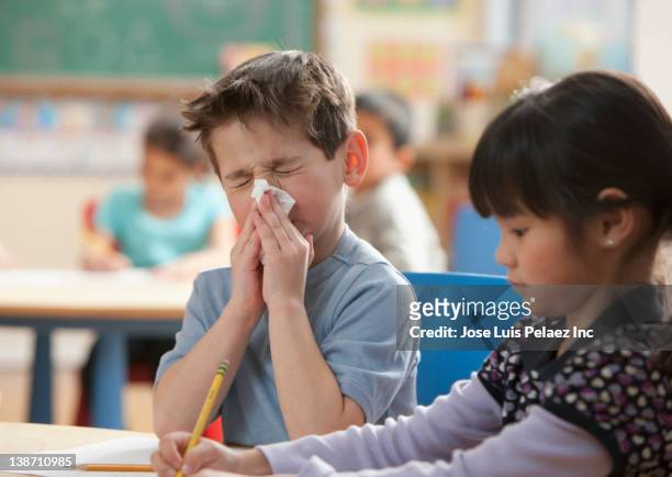 caucasian boy blowing nose in classroom - influenza virus foto e immagini stock