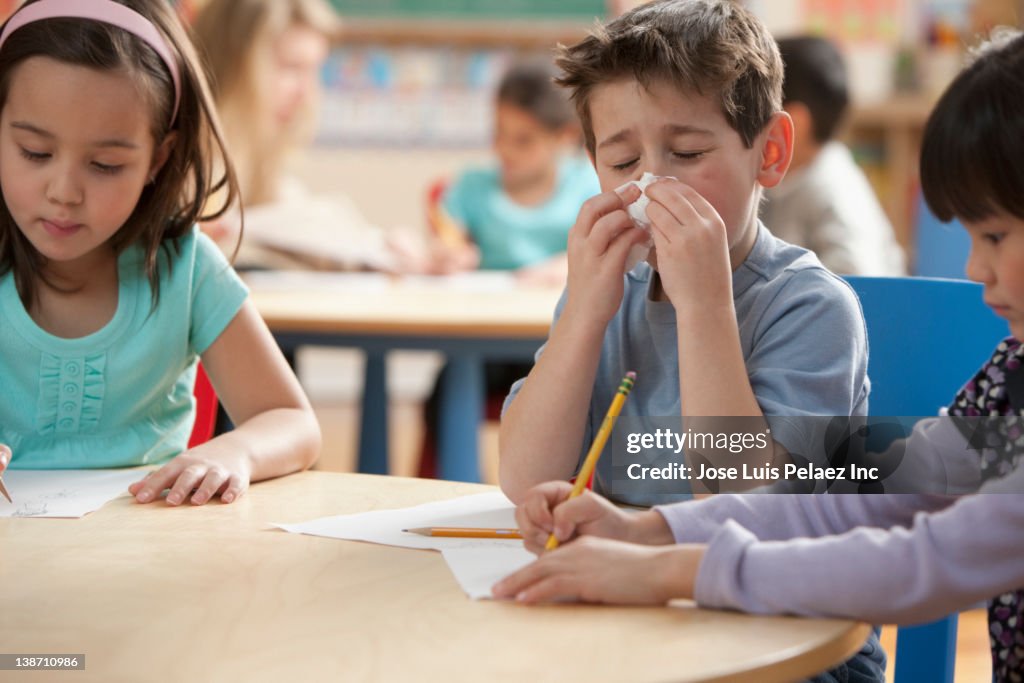 Caucasian boy blowing nose in classroom
