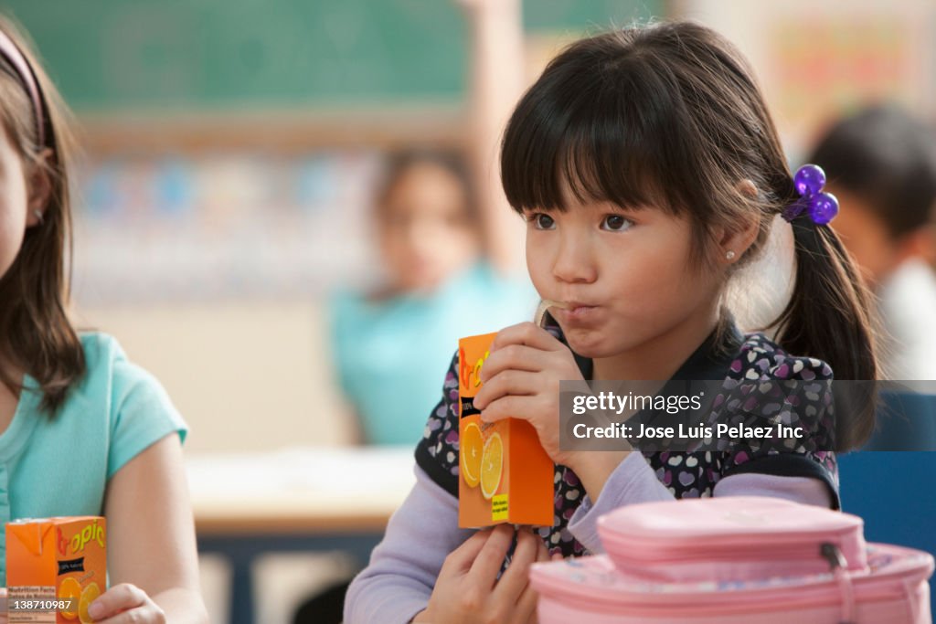 Asian girl drinking juice in classroom