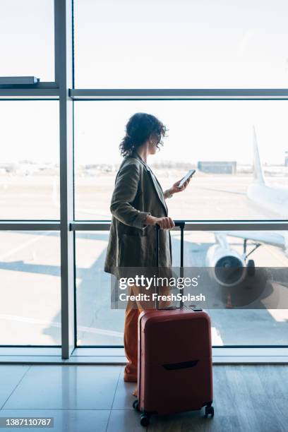 eine seitenansicht einer unkenntlich beschäftigten, eleganten geschäftsfrau, die ihr mobiltelefon benutzt, um mit ihren geschäftspartnern zu sprechen, während sie auf ihren flug wartet - airport smartphone stock-fotos und bilder