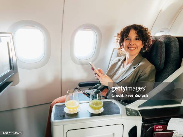 eine kaukasische frau, die lächelt und in die kamera schaut, während sie in einem flugzeug sitzt und ihr handy hält und ihre überseereise genießt - airplane food stock-fotos und bilder