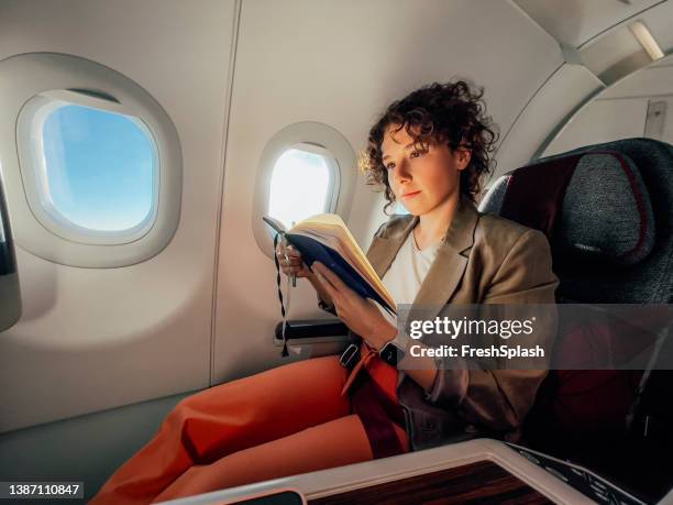 a beautiful businesswoman reading her notes while travelling by plane - business woman blue stock pictures, royalty-free photos & images