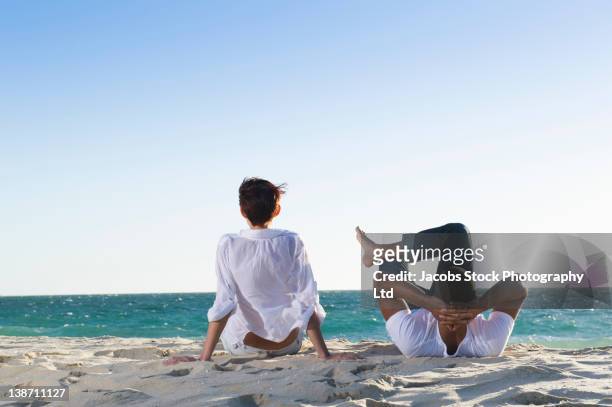 mixed race couple sitting on beach - lying on back ストックフォトと画像