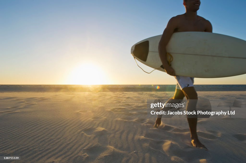 Mixed race man running on beach with surfboard