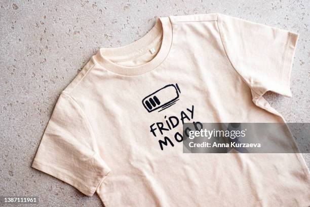 close-up of beige t-shirt with a print “friday mood” on light background, top view - white shirt template stock pictures, royalty-free photos & images