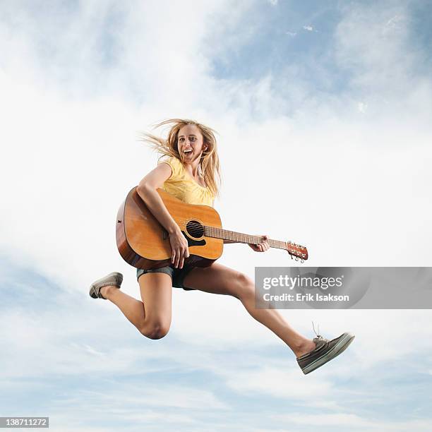 caucasian woman jumping in mid-air playing guitar - air guitar stockfoto's en -beelden