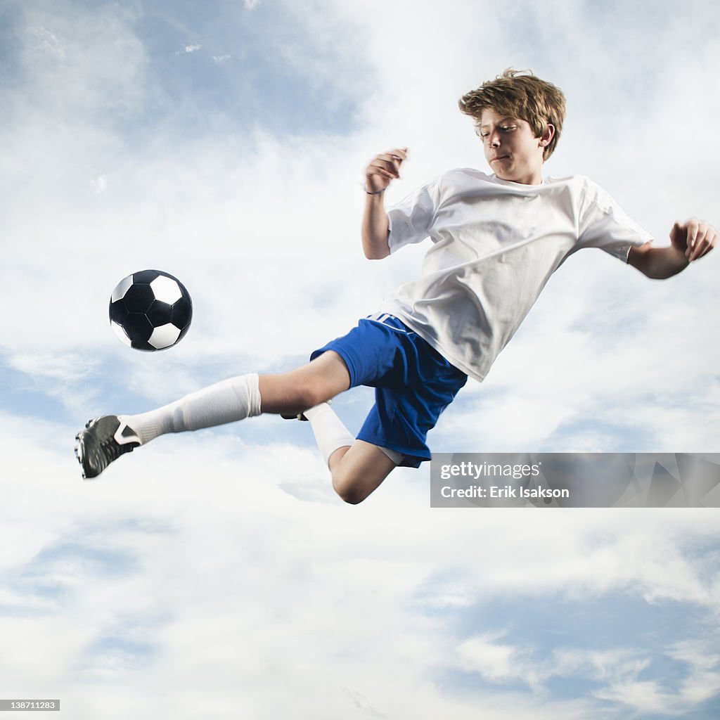 Caucasian teenager kicking soccer ball in mid-air