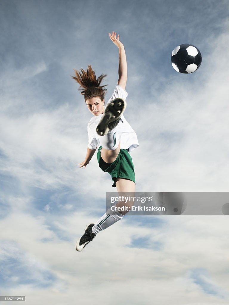Caucasian teenager kicking soccer ball in mid-air