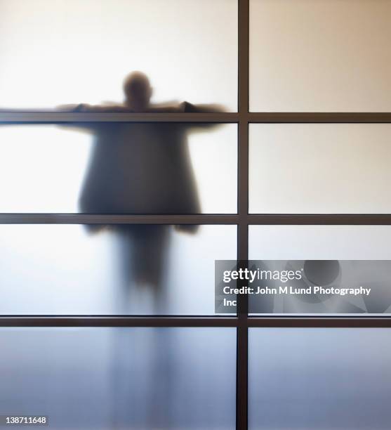 businessman standing behind glass wall in office - head in hands silhouette stock pictures, royalty-free photos & images