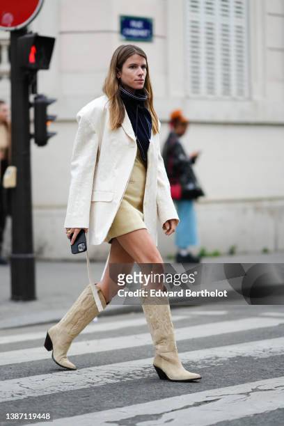 Monica Ainley wears a navy blue with white seams high neck, a beige short skirt, a white latte embossed striped pattern oversized blazer jacket, gold...