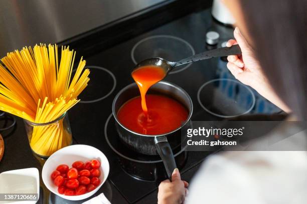 high angle, over the shoulder view of a woman stirring boiling soup from saucepanwith tomato - sauce stockfoto's en -beelden