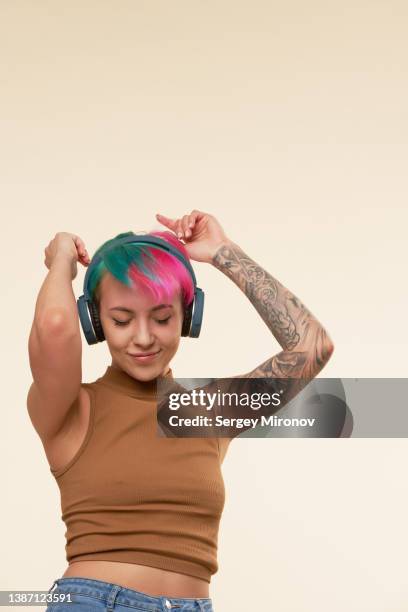 young attractive woman with green and pink hairs dancing with headphones - female body piercing fotografías e imágenes de stock