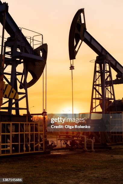 the silhouette of two oil pumps on a beautiful sunset sky with sun setting in between them. - oil pump stock pictures, royalty-free photos & images