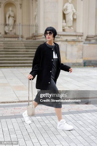 Model and artist Zoe Helali wearing a dark grey t-shirt dress with tigh high slit by Iro, a black jacket by Iro, sunglasses by Hies Optik, a beige...