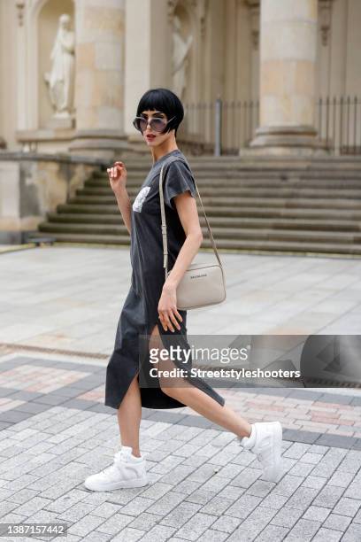 Model and artist Zoe Helali wearing a dark grey t-shirt dress with tigh high slit by Iro, sunglasses by Hies Optik, a beige bag by Balenciaga and...